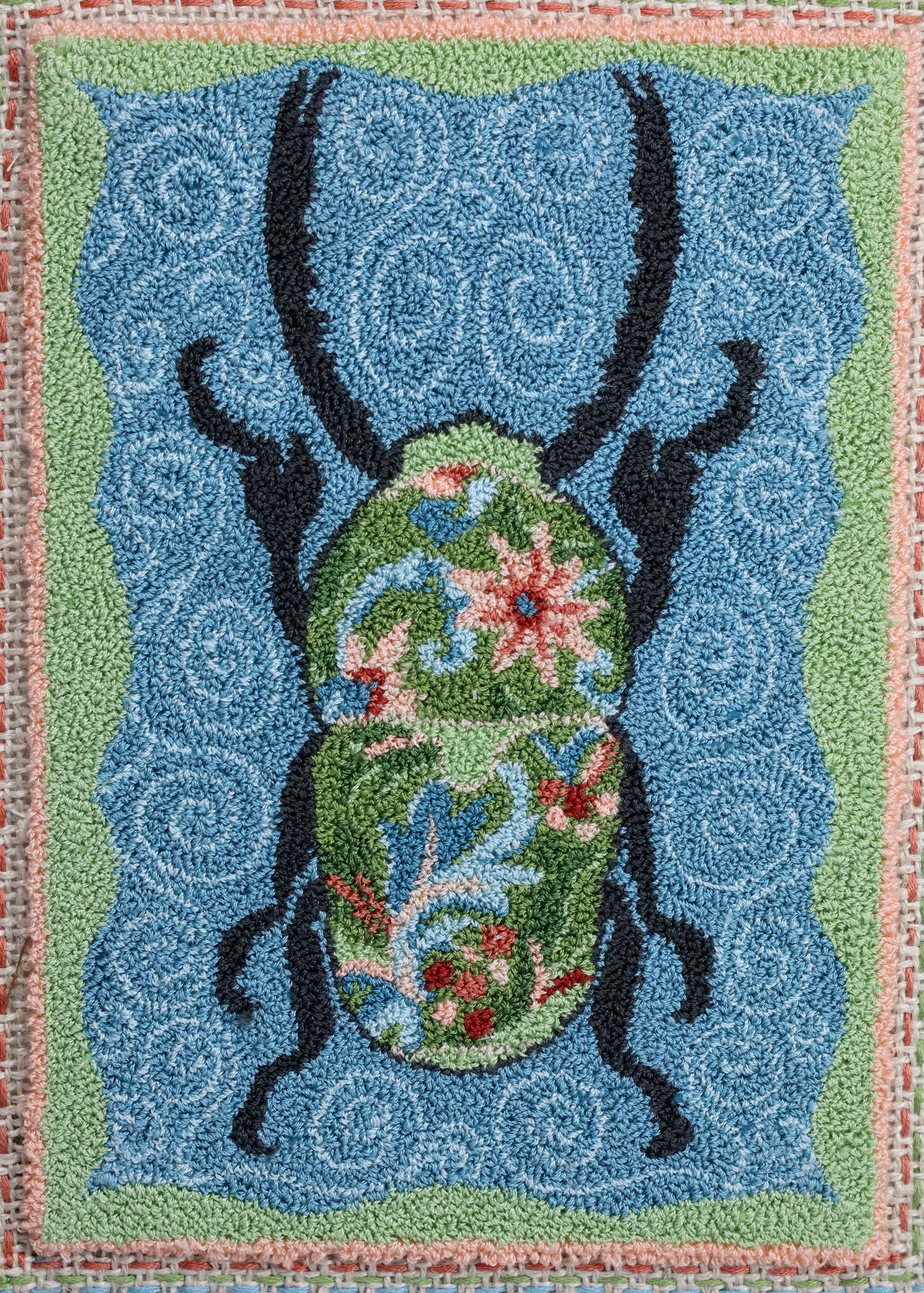 Punch Needle Embroidery artwork of a beetle with a floral design on a blue background, framed in black.