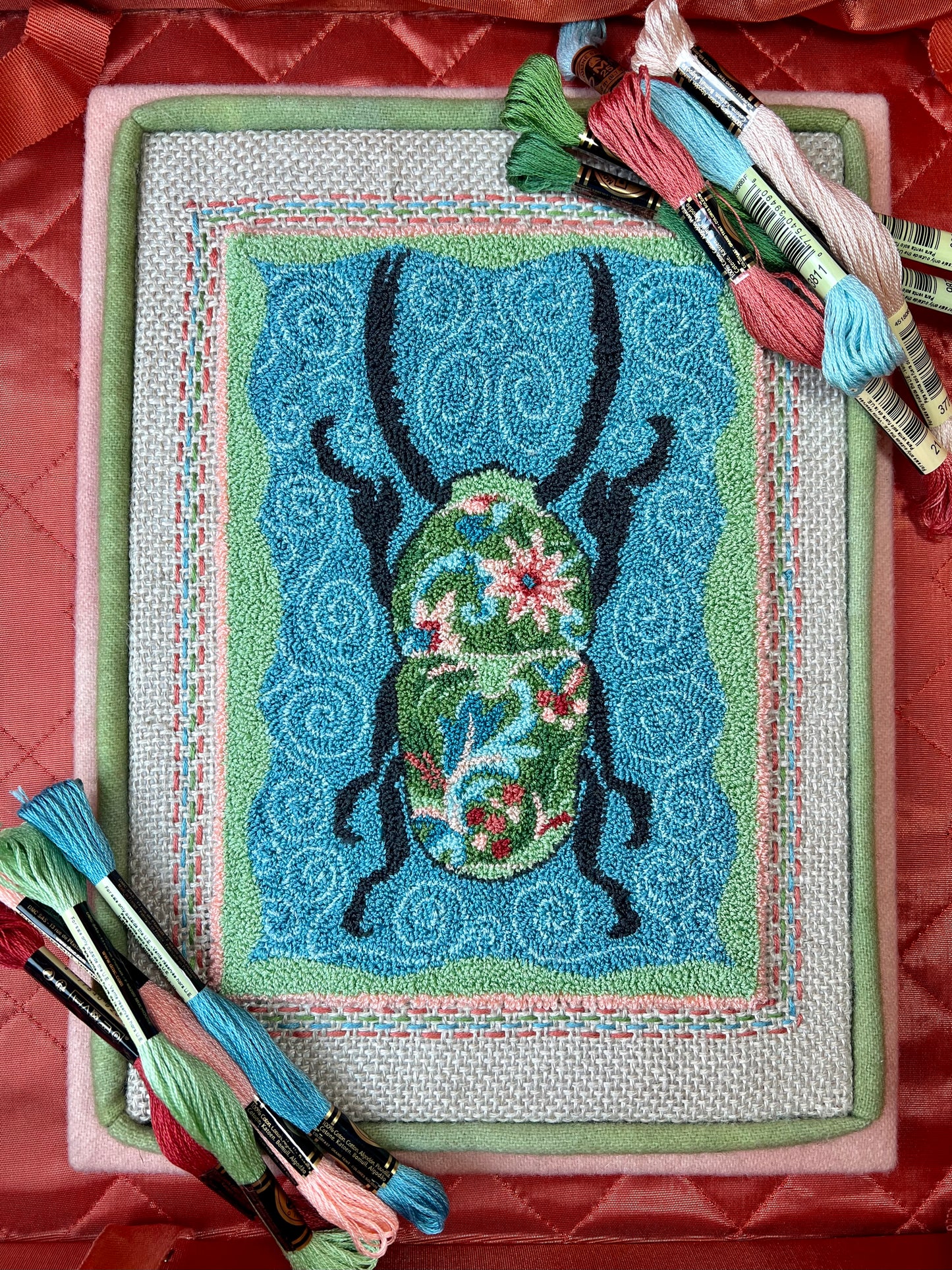 Punch Needle Embroidery artwork of a beetle with a floral design on a blue background, framed in black.