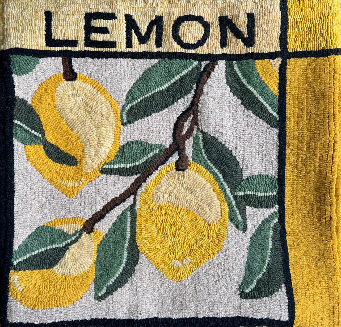 Lemon rug hooking pattern by Orphaned Wool, copyright © 2025 Kelly Kanyok. This picture shows the finished design enlarged 300% to create a beautiful pillow. The design features three lemons with the word "lemon" on top.