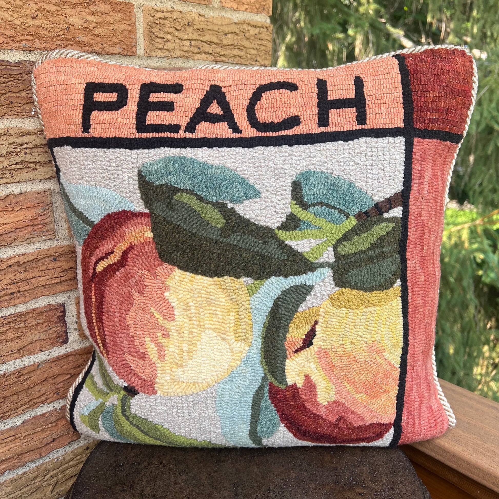Peach paper rug hooking pattern by Orphaned Wool, copyright © 2025 Kelly Kanyok. This paper pattern is designed to be enlarged. This picture shows the finished design enlarged 300% to create a beautiful pillow. The design features two peaches with the word peach on the top. This pattern is one of four fruit patterns available. sold individually or as a set of four. Lemon, Lime, Peach and Cherry designs.